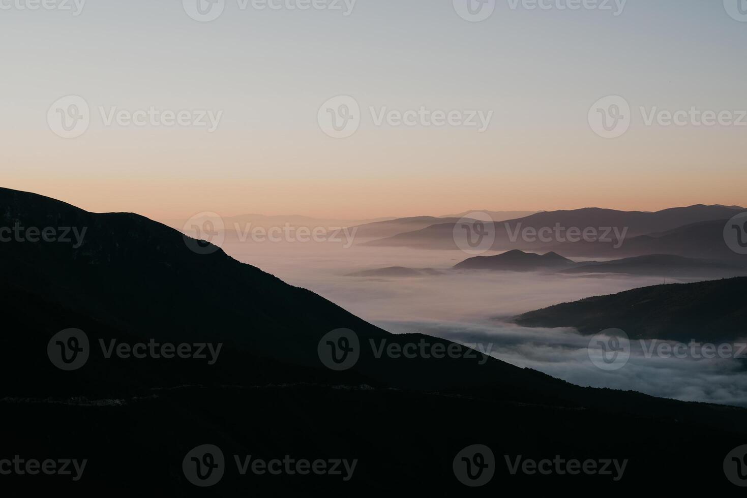 Mountain range with visible silhouettes through the morning colorful fog photo