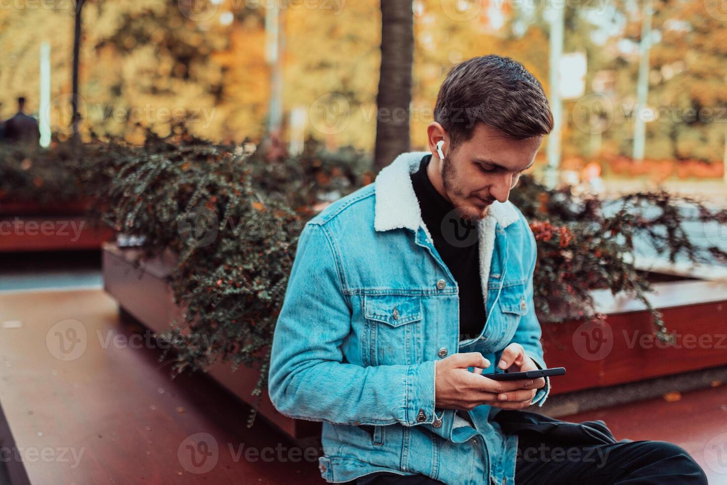 A gappy student sitting in a park using a smartphone and wireless headphones photo