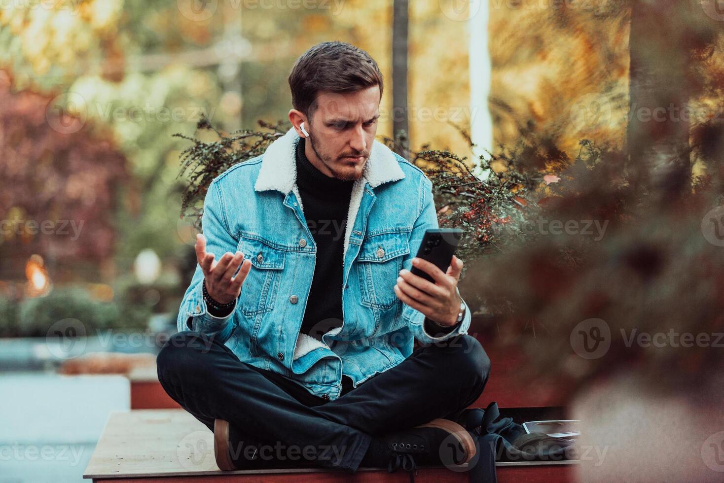 A gappy student sitting in a park using a smartphone and wireless headphones photo