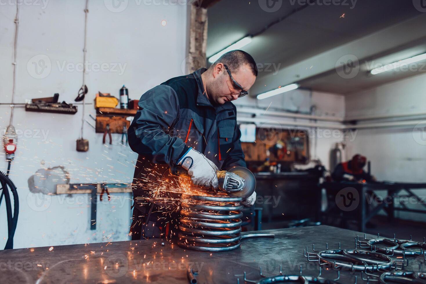 Locksmith in special clothes and goggles works in production. Metal processing with angle grinder. Sparks in metalworking. photo