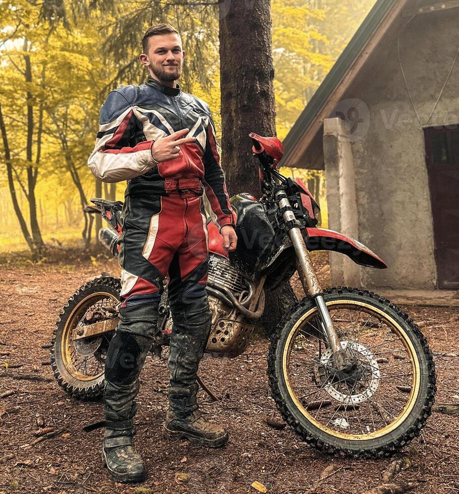 A professional motorcyclist resting on a forest road after an adventurous ride photo