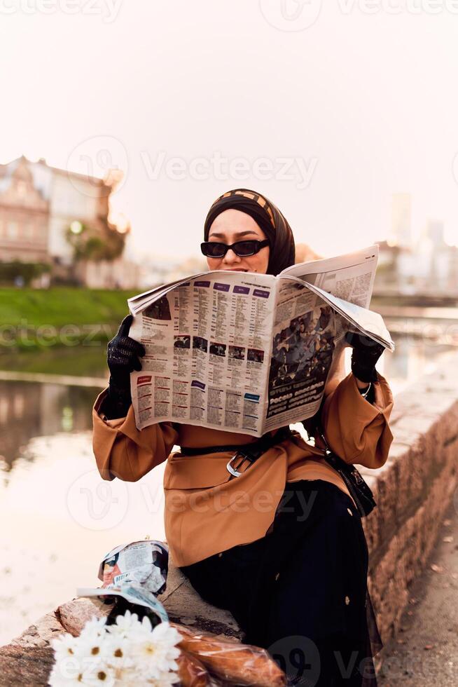 A woman in a hijab gracefully adorned in a fusion of old and modern French attire, immersed in the bustling streets of the city, engrossed in reading a newspaper photo