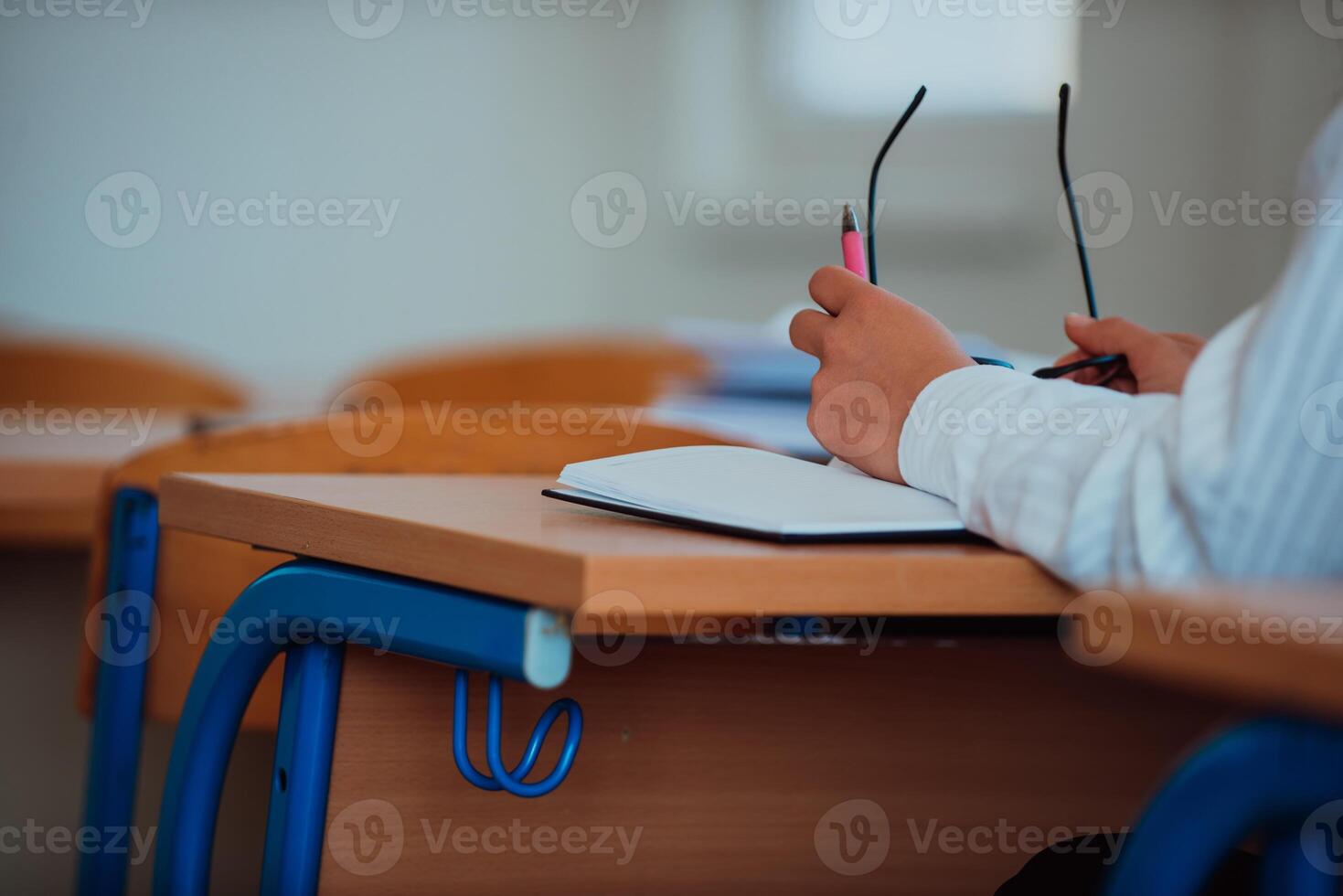 A close-up a student in a classroom holding glasses in her hand while focusing on her academic studies. photo