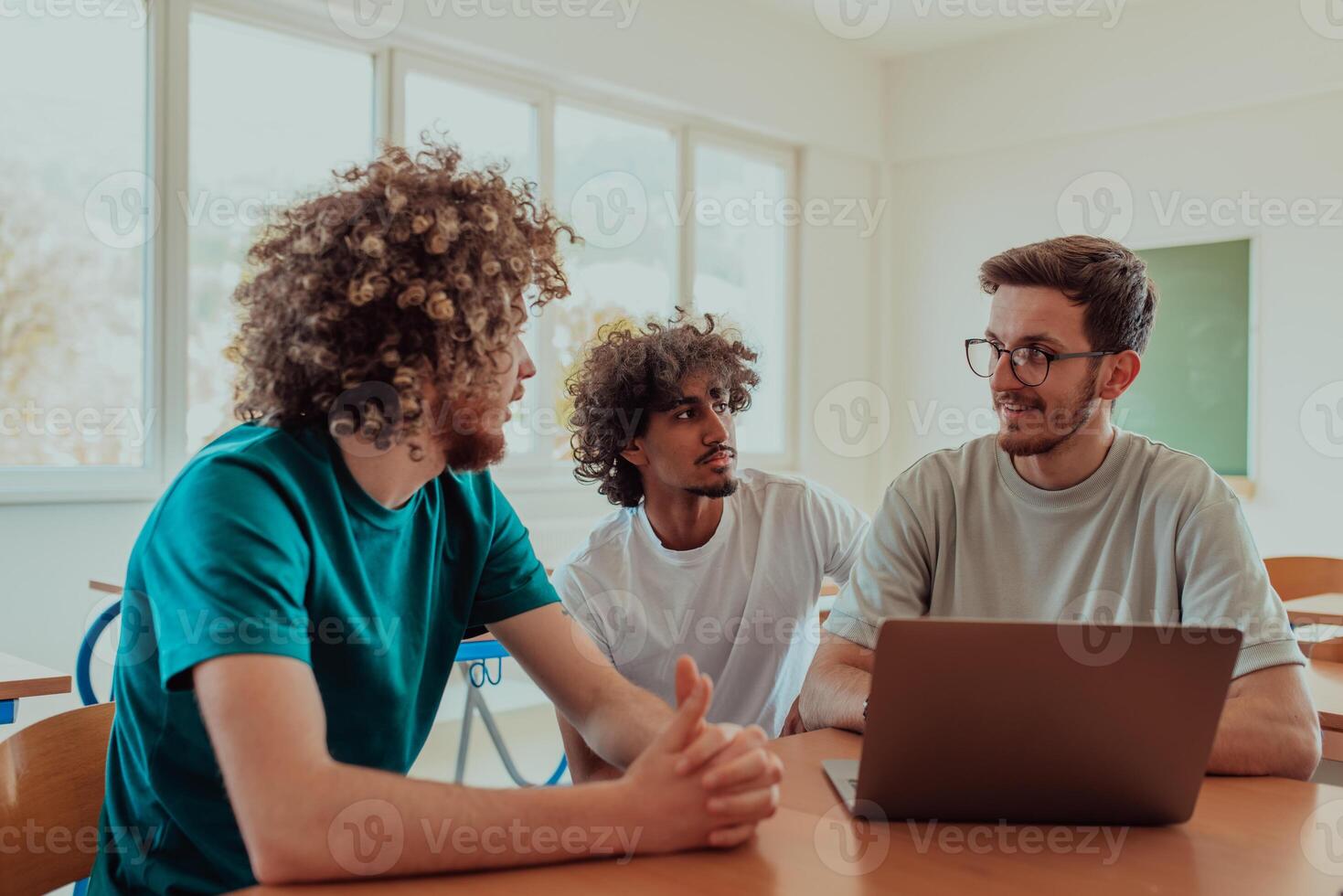 Group students including one African-American, sit together in a classroom, engaging in a discussion while reviewing information on a laptop photo