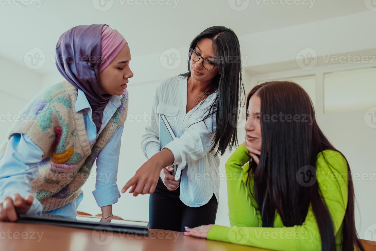Group of business woman one of them is wearing a hijab, are reviewing papers and a laptop together, creating new business projects, demonstrating teamwork, collaboration, and productivity. photo