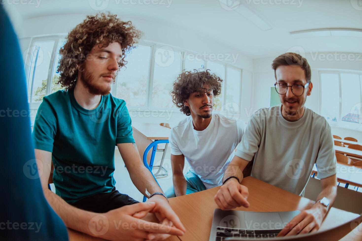 A diverse studetns group, including an Afro American with an afro hairstyle communicating and engage with their colleague while seated in a modern classroom, collectively focused on a laptop. photo