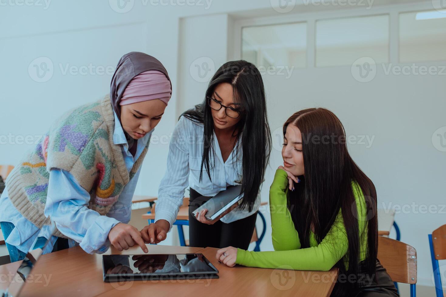Group of business woman one of them is wearing a hijab, are reviewing papers and a laptop together, creating new business projects, demonstrating teamwork, collaboration, and productivity. photo