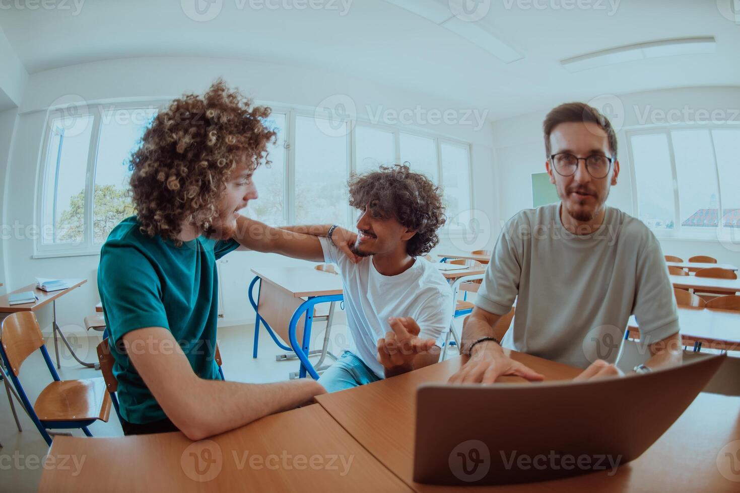 A diverse studetns group, including an Afro American with an afro hairstyle communicating and engage with their colleague while seated in a modern classroom, collectively focused on a laptop. photo