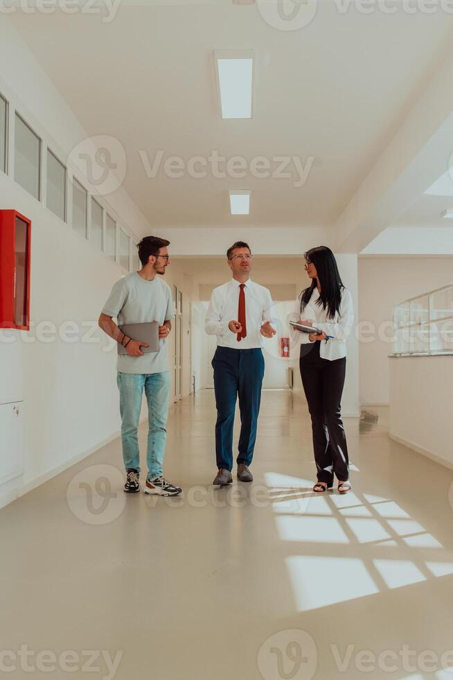 The director conducts a conversation with the secretary and a young programmer in a modern and spacious corridor of a large company, discussing various business topics and projects. photo