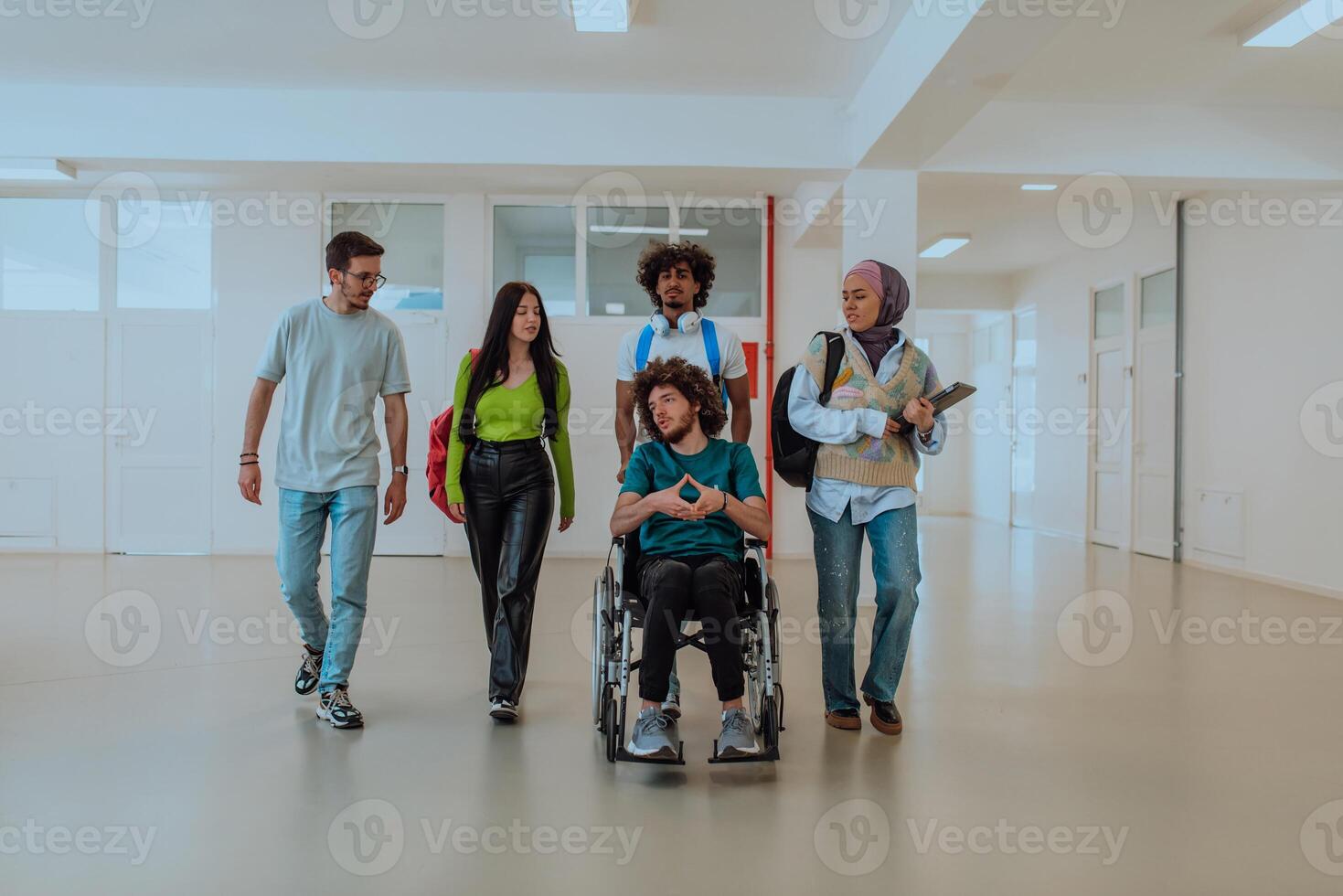 In a modern university, a diverse group of students, including an African American student and a hijab-wearing woman, walk together in the hallway, accompanied by their wheelchair-bound colleague. photo