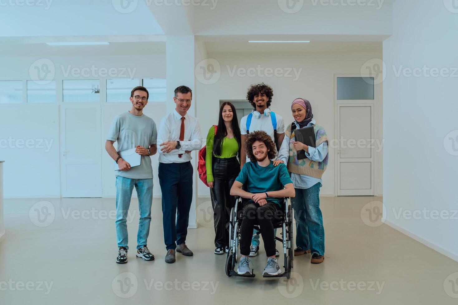 A group of students with a professor and a colleague who is in a wheelchair are standing together in the corridor of a modern university photo