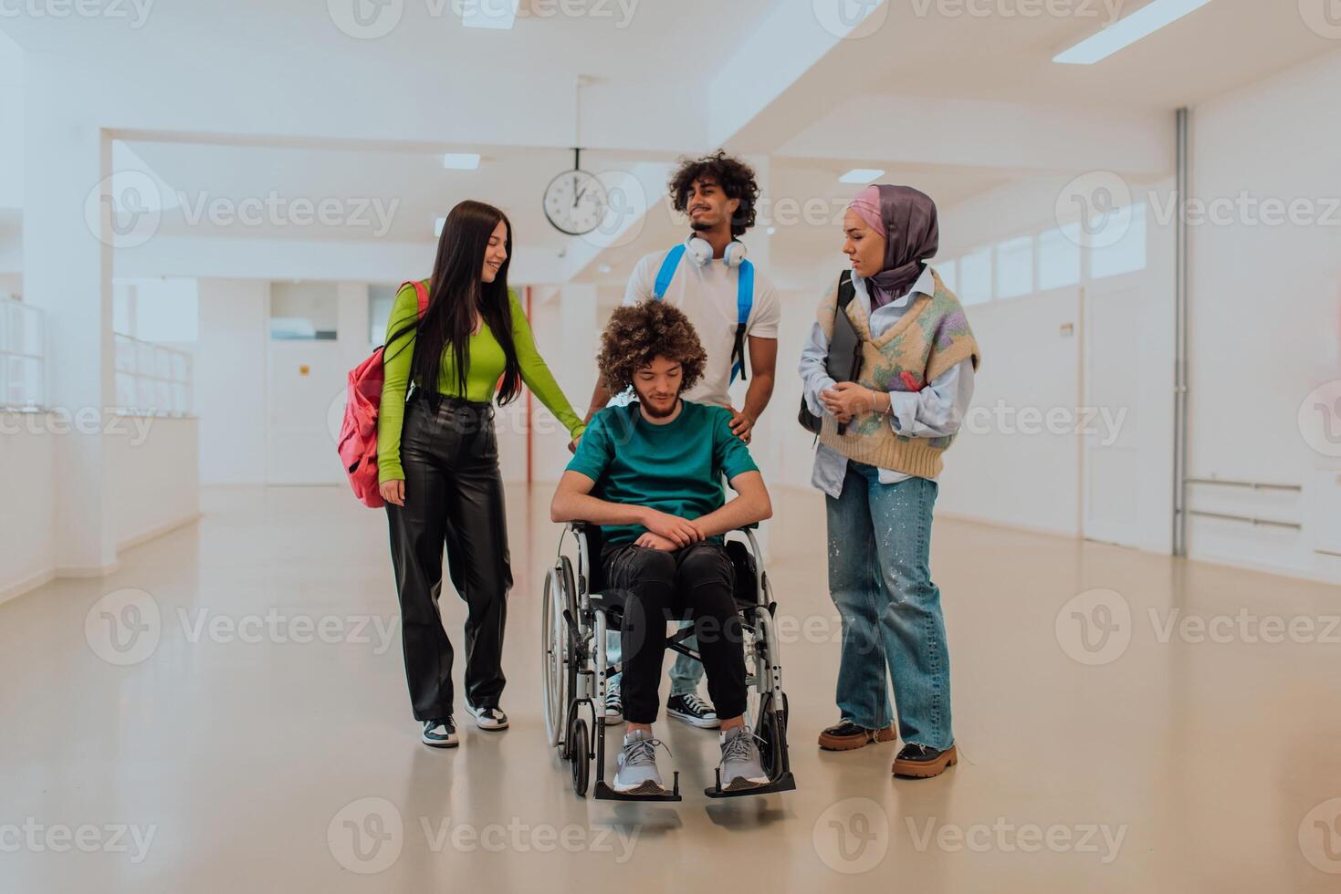 In a modern university, a diverse group of students, including an African American student and a hijab-wearing woman, walk together in the hallway, accompanied by their wheelchair-bound colleague photo