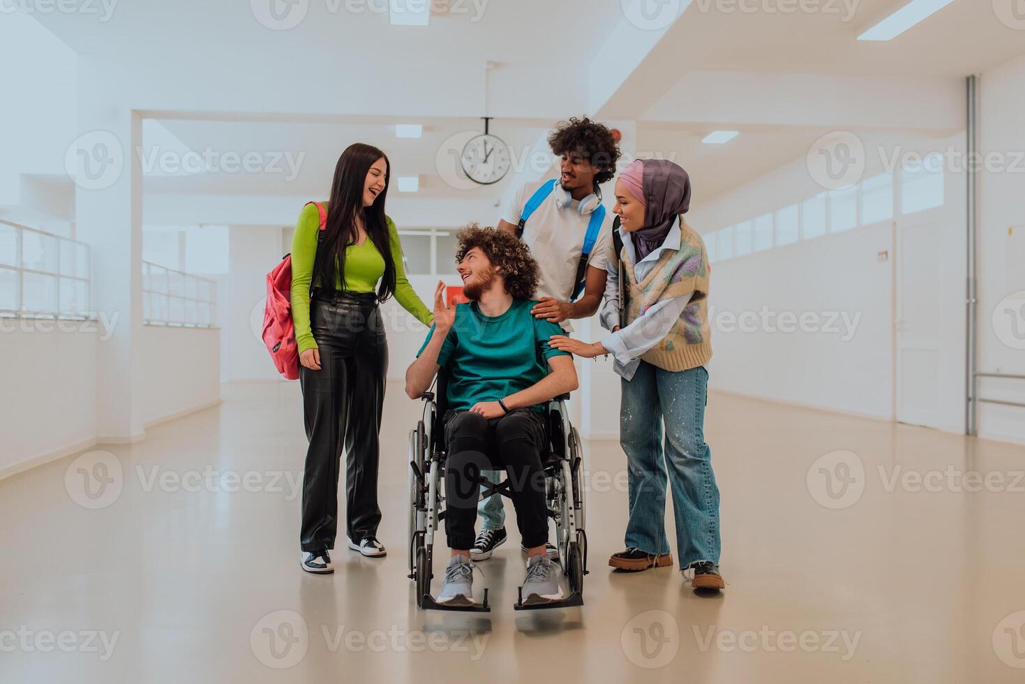 In a modern university, a diverse group of students, including an African American student and a hijab-wearing woman, walk together in the hallway, accompanied by their wheelchair-bound colleague photo