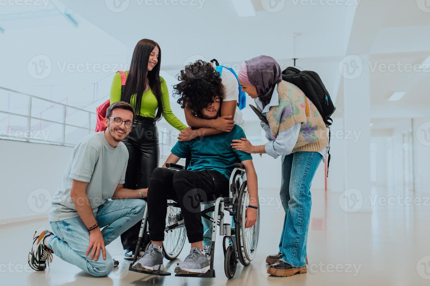 In a modern university, a diverse group of students, including an African American student and a hijab-wearing woman, walk together in the hallway, accompanied by their wheelchair-bound colleague photo