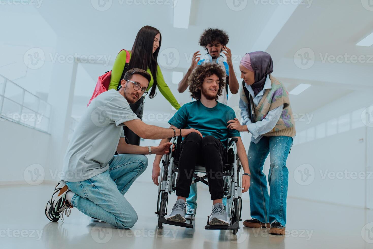 In a modern university, a diverse group of students, including an African American student and a hijab-wearing woman, walk together in the hallway, accompanied by their wheelchair-bound colleague photo