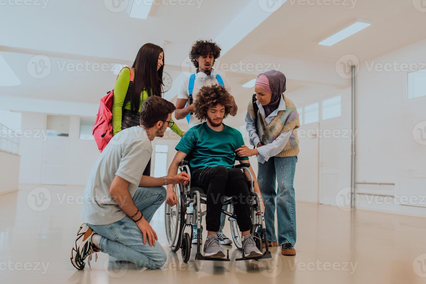 In a modern university, a diverse group of students, including an African American student and a hijab-wearing woman, walk together in the hallway, accompanied by their wheelchair-bound colleague photo