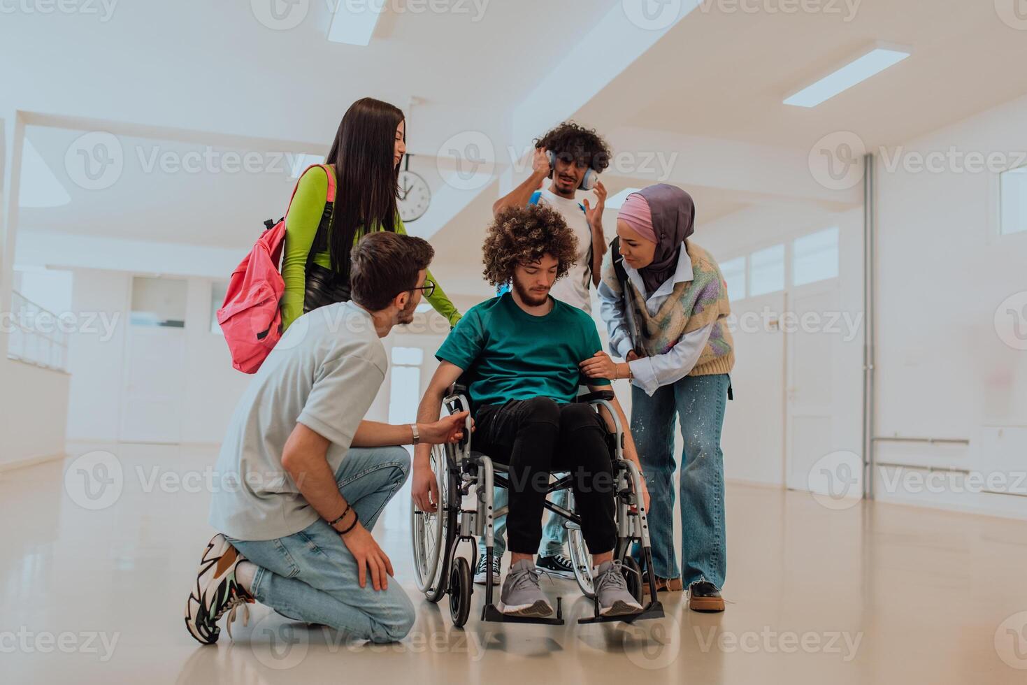 In a modern university, a diverse group of students, including an African American student and a hijab-wearing woman, walk together in the hallway, accompanied by their wheelchair-bound colleague photo