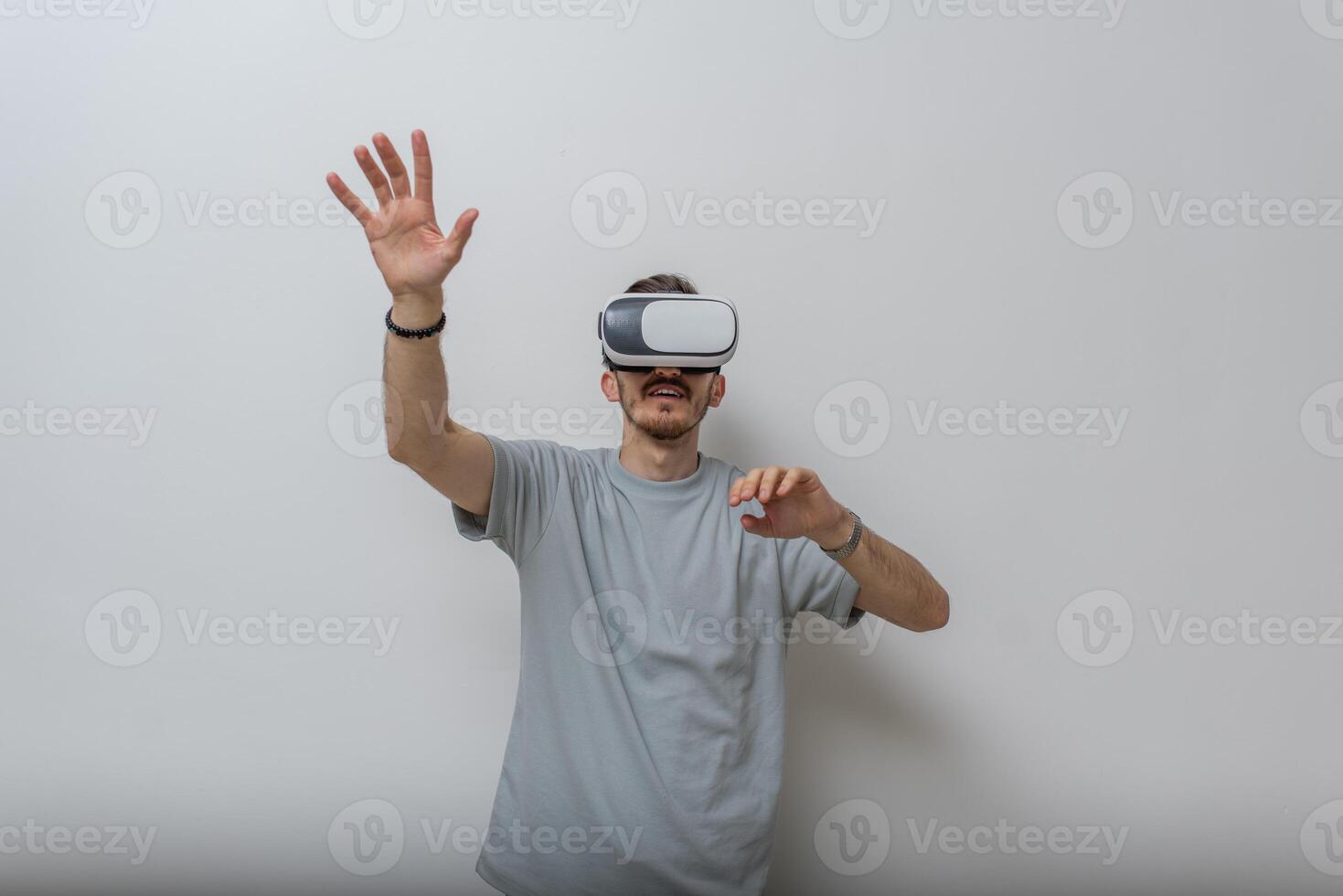 Futuristic man wearing virtual reality glasses interacts with the air in an isolated gray background. photo