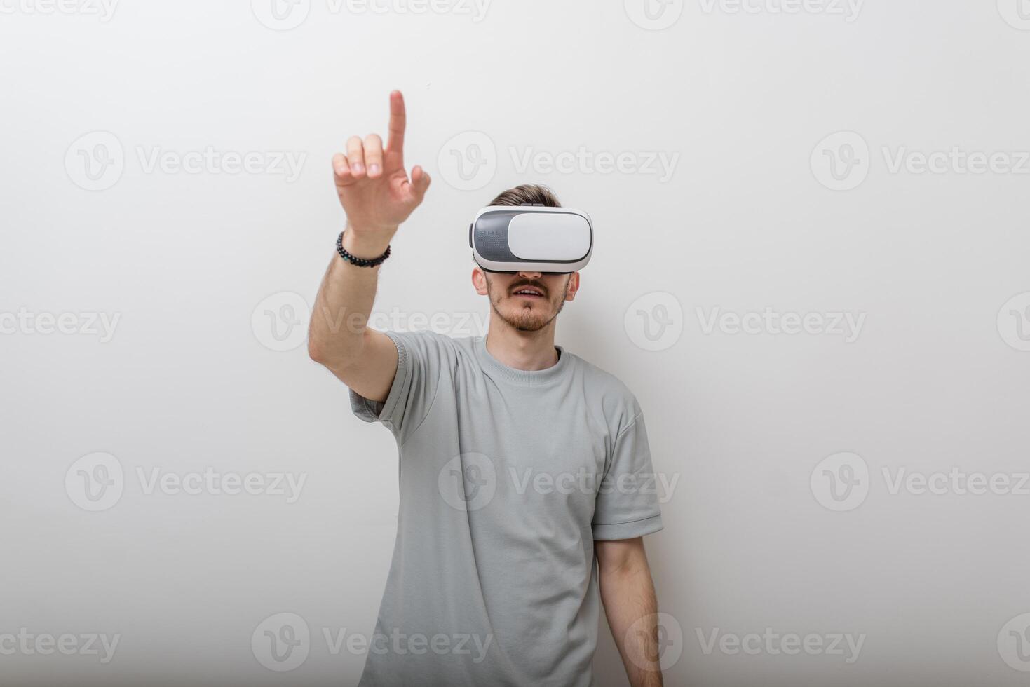 Futuristic man wearing virtual reality glasses interacts with the air in an isolated gray background. photo