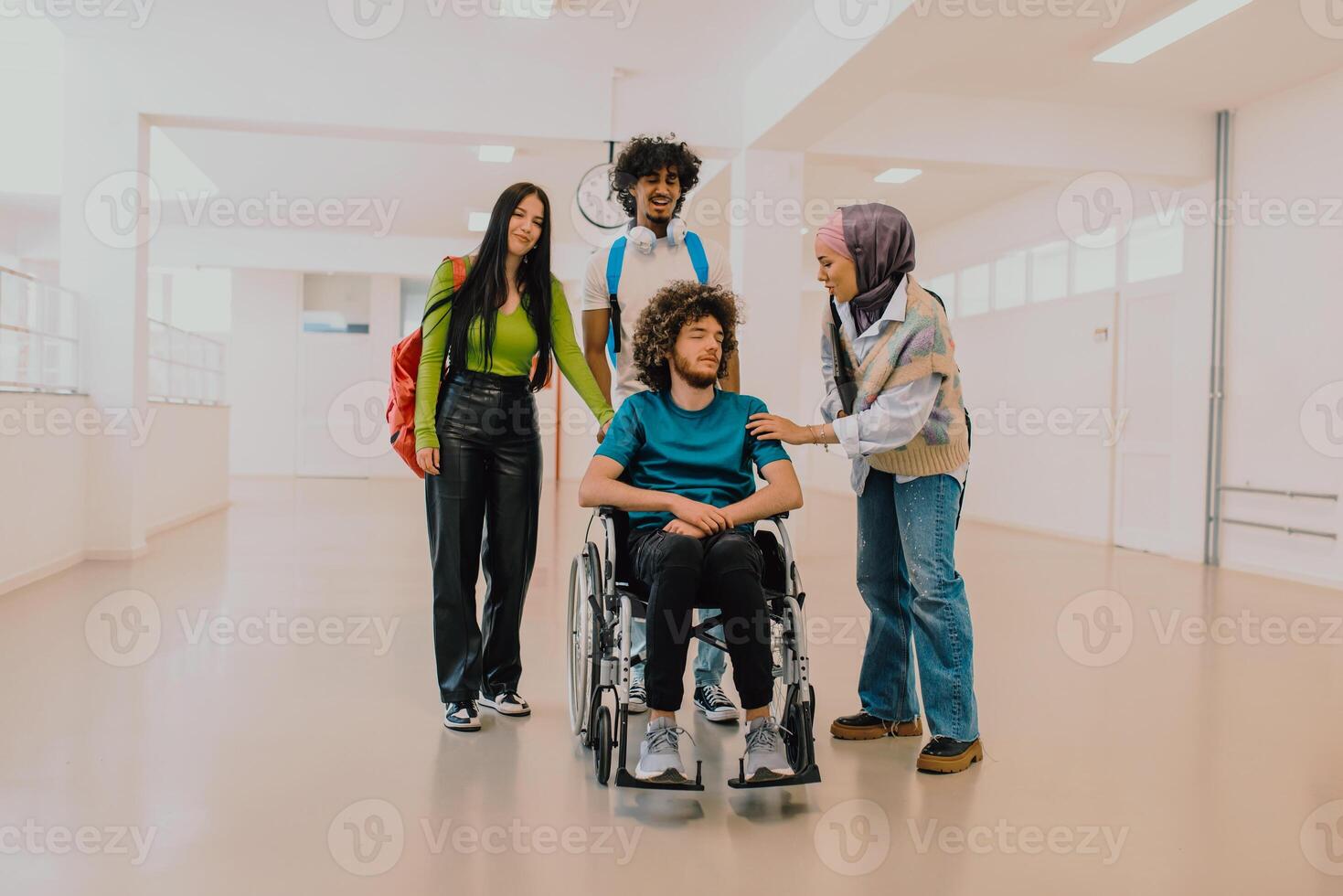 In a modern university, a diverse group of students, including an African American student and a hijab-wearing woman, walk together in the hallway, accompanied by their wheelchair-bound colleague photo