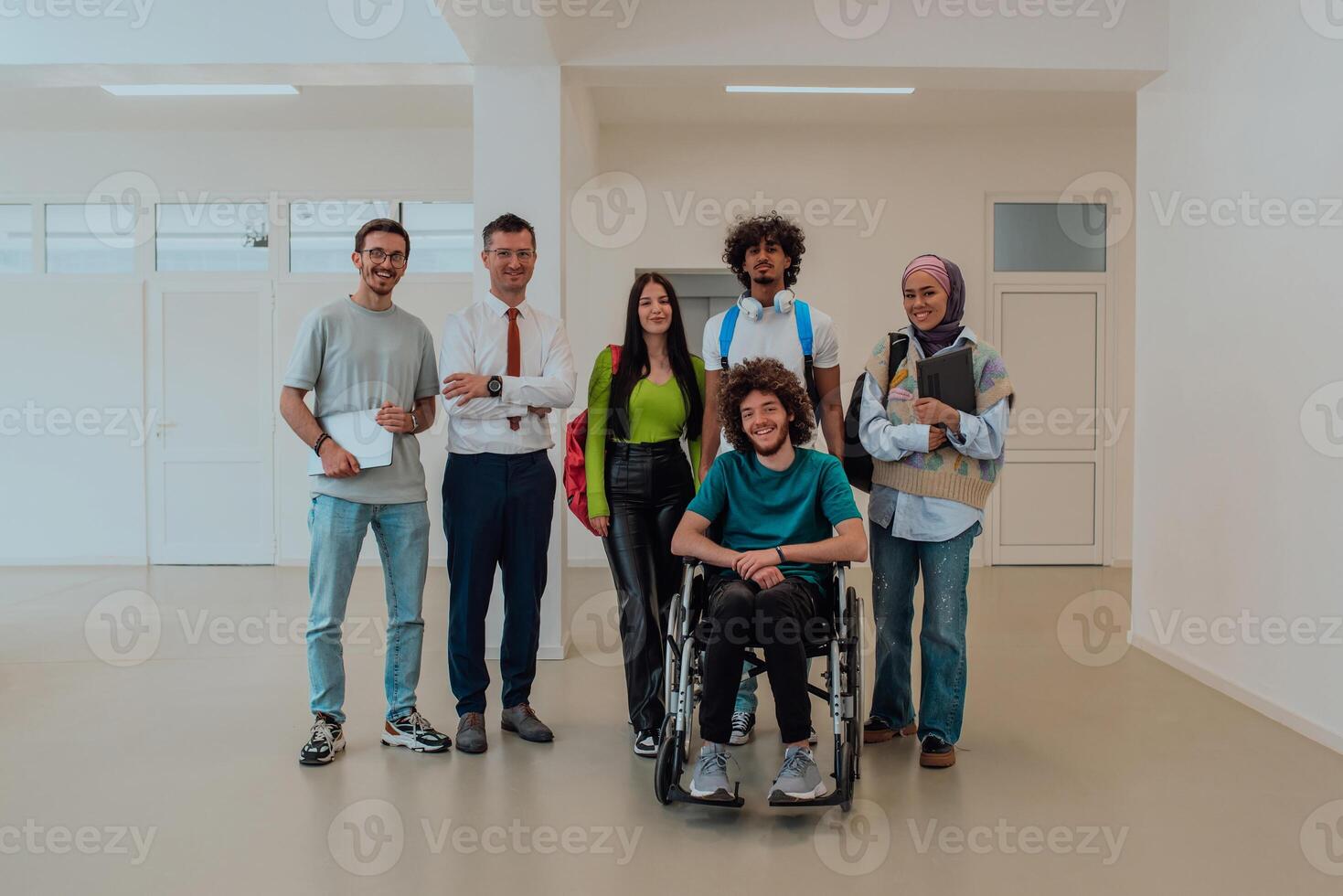 A group of students with a professor and a colleague who is in a wheelchair are standing together in the corridor of a modern university photo