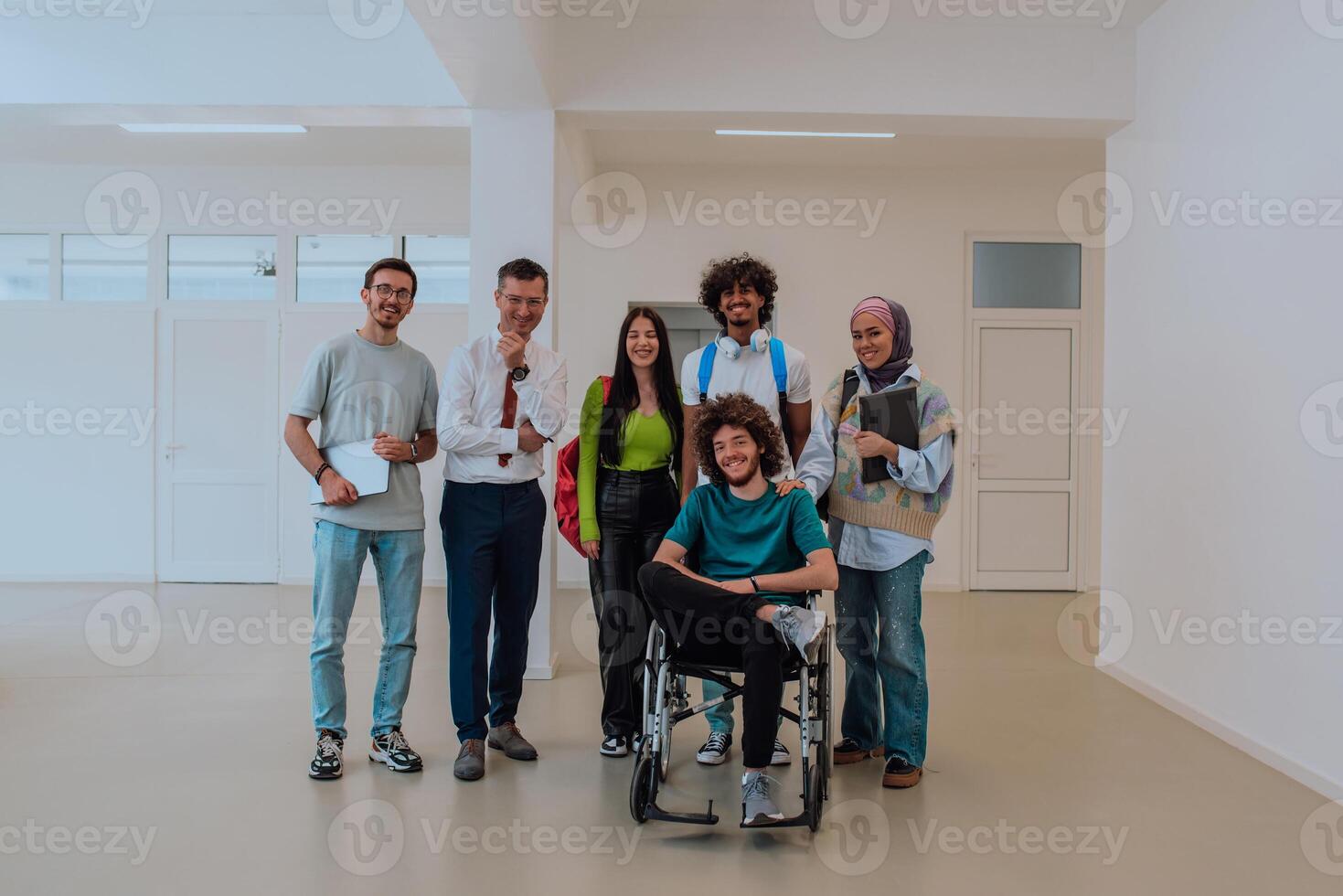 A group of students with a professor and a colleague who is in a wheelchair are standing together in the corridor of a modern university photo