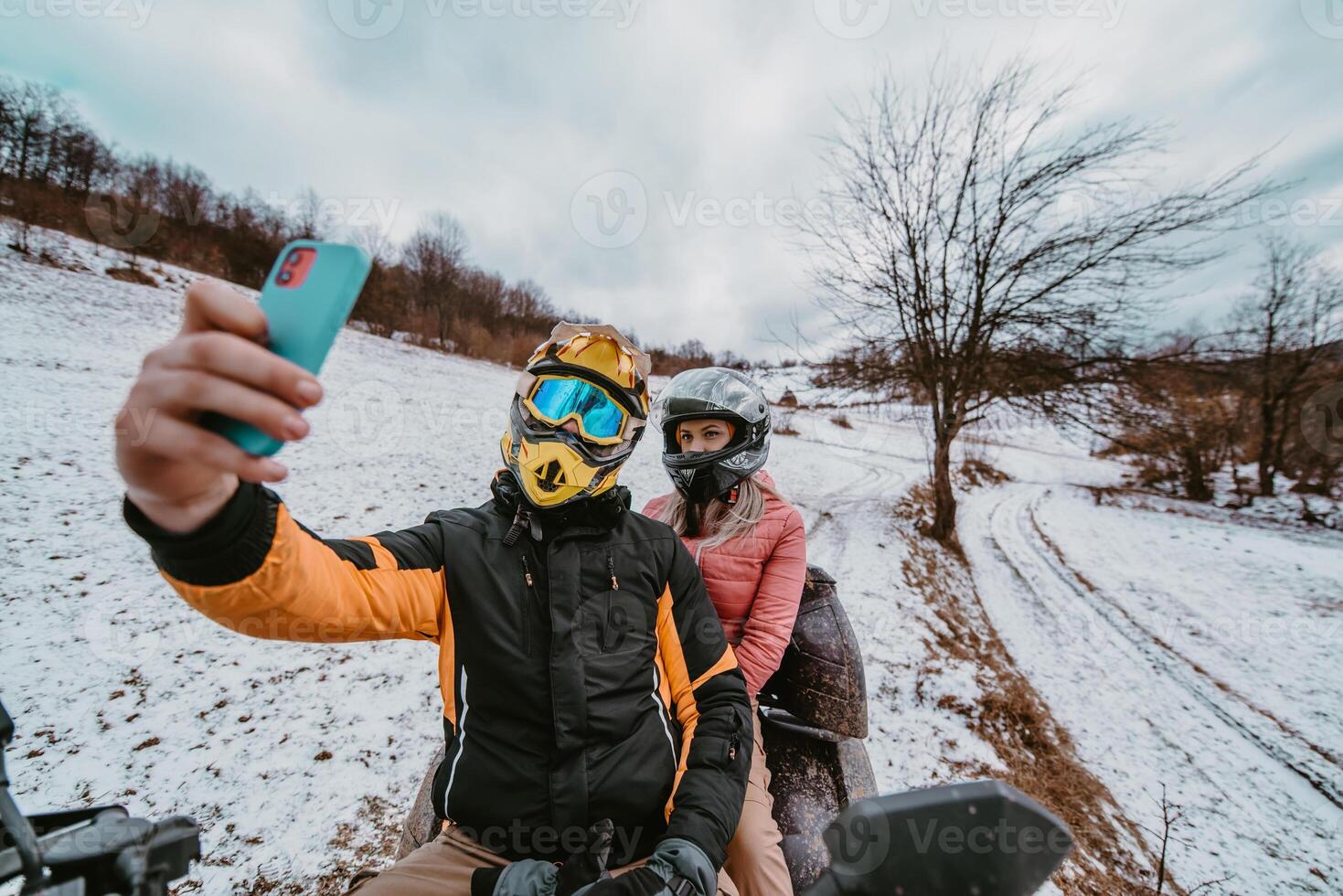A couple enjoys an adventurous quad ride through the snowy landscape, capturing the thrill of the moment with a selfie on their smartphone amidst the wintry wonderland photo