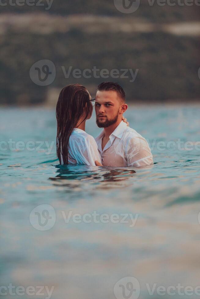 A symbolic and emotionally connected couple tenderly embraces against the backdrop of a serene sea, bathed in the warm hues of a breathtaking sunset photo