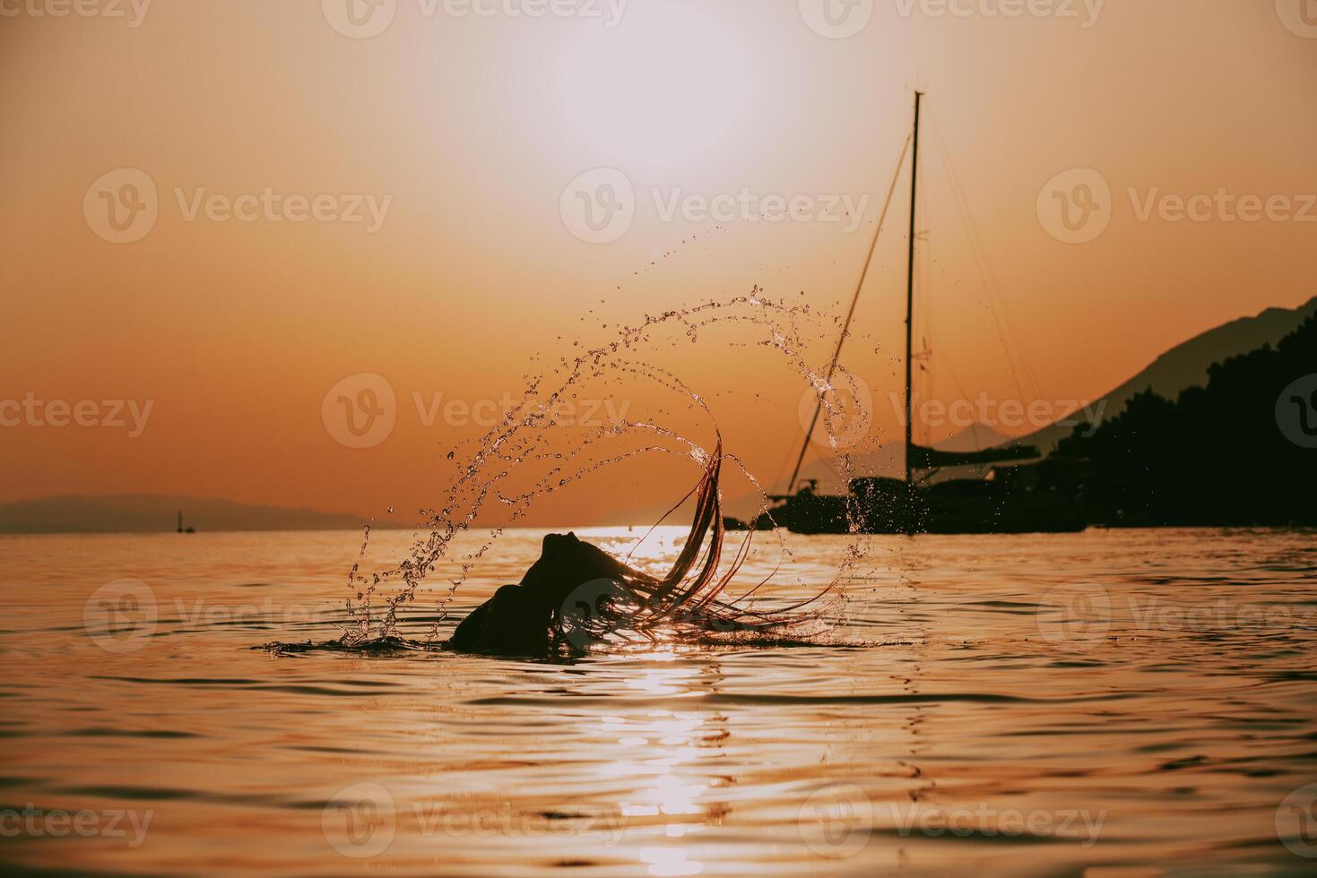 Silhouette of a woman enjoying a playful moment in the sea during sunset, her hair blowing in the wind, capturing the essence of carefree beach fun photo