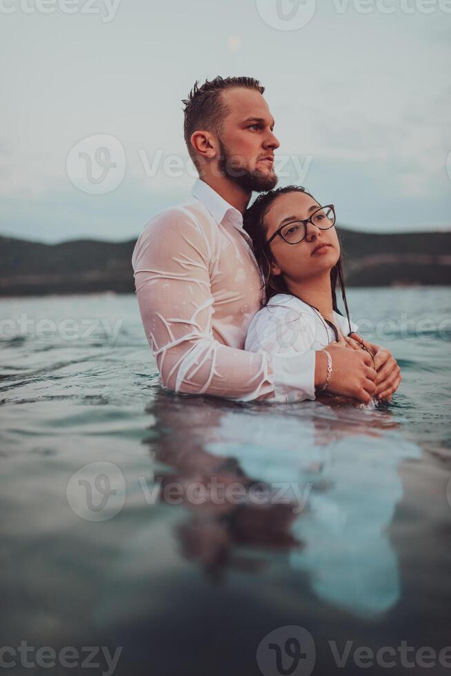 A symbolic and emotionally connected couple tenderly embraces against the backdrop of a serene sea, bathed in the warm hues of a breathtaking sunset photo