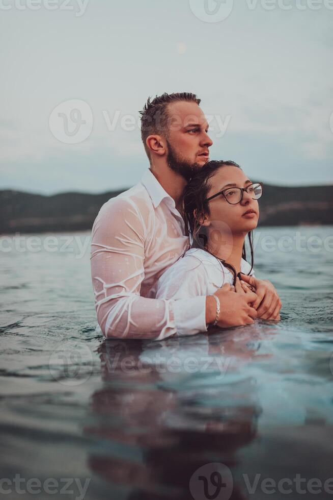 A symbolic and emotionally connected couple tenderly embraces against the backdrop of a serene sea, bathed in the warm hues of a breathtaking sunset photo