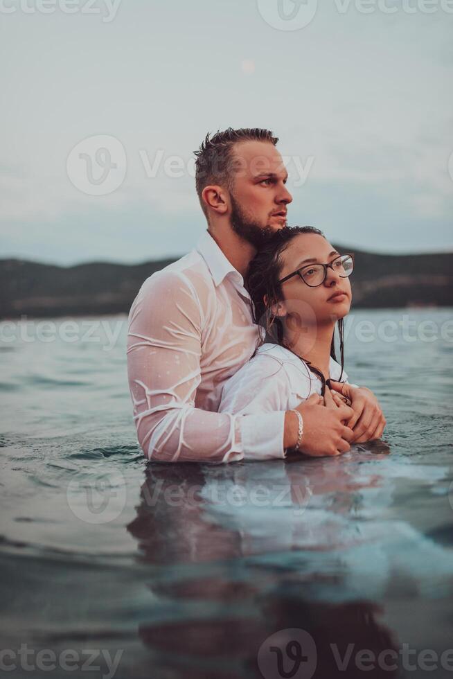 A symbolic and emotionally connected couple tenderly embraces against the backdrop of a serene sea, bathed in the warm hues of a breathtaking sunset photo