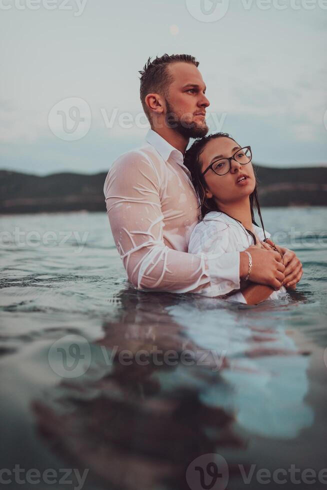A symbolic and emotionally connected couple tenderly embraces against the backdrop of a serene sea, bathed in the warm hues of a breathtaking sunset photo