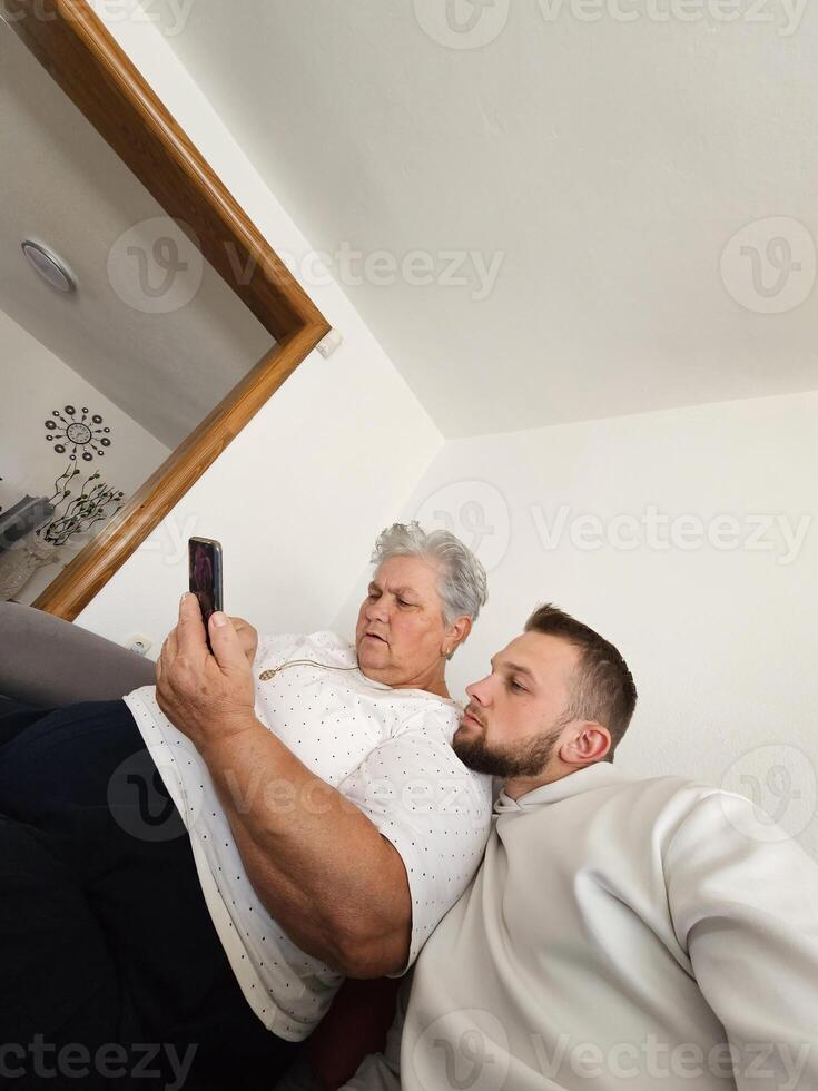 A heartwarming, real-life moment captured. A young boy and his grandmother, sitting together, joyfully exploring a smartphone as they bridge generations with love and technology photo