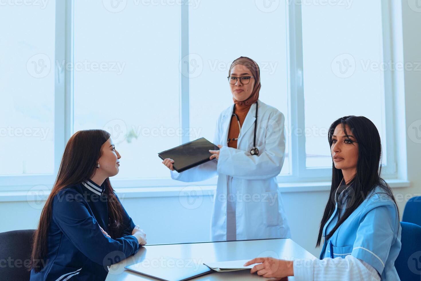 A successful doctor in a hijab confidently presents her work plan to colleagues in a hospital, while using a smart tablet to enhance patient care and communication in the healthcare facility photo