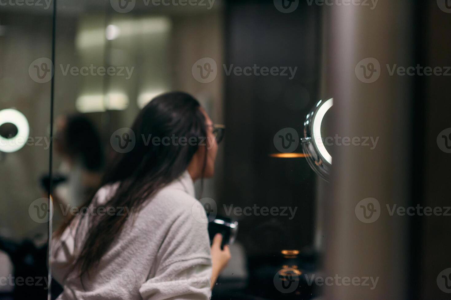 A joyful woman, with headphones in her ears, playfully dries her hair with a hairdryer in the bathroom after a refreshing bath, embodying a carefree and energetic moment of self-care and relaxation photo