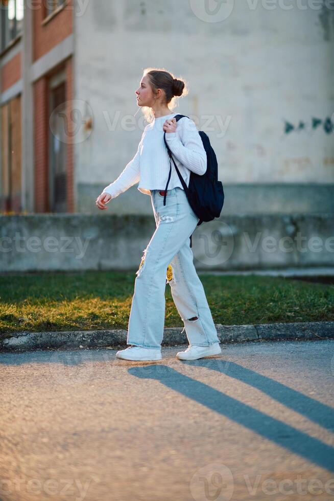 A beautiful European teenager, captured in a side-profile portrait, walks home during sunset after school, carrying her backpack photo