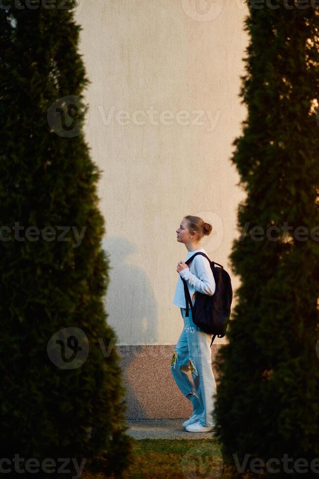 A beautiful European teenager, captured in a side-profile portrait, walks home during sunset after school, carrying her backpack photo