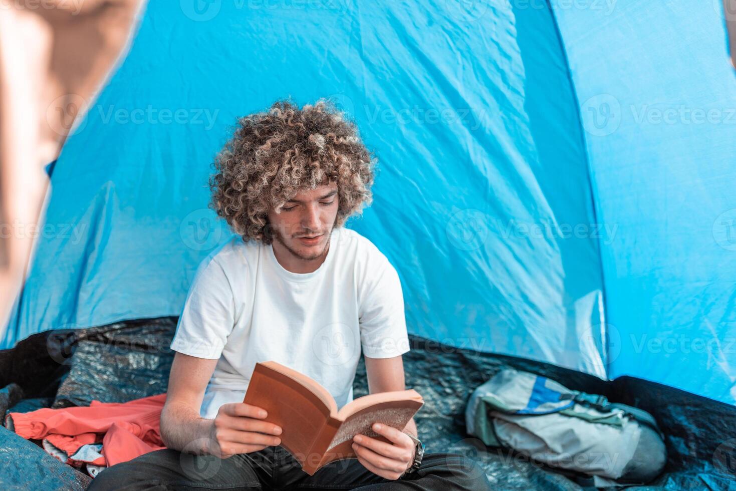 An afro teenager relaxes in a mountaineering tent while reading a book photo