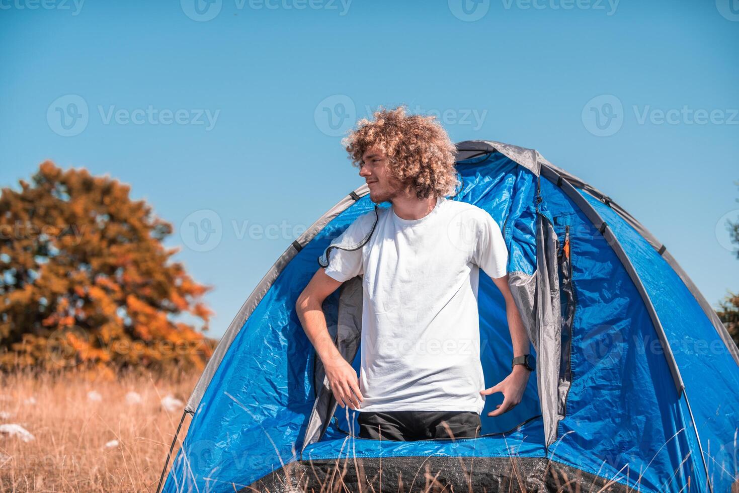 A man with a tent enjoys a sunny day whileusing a smartphone and camping in the mountains photo