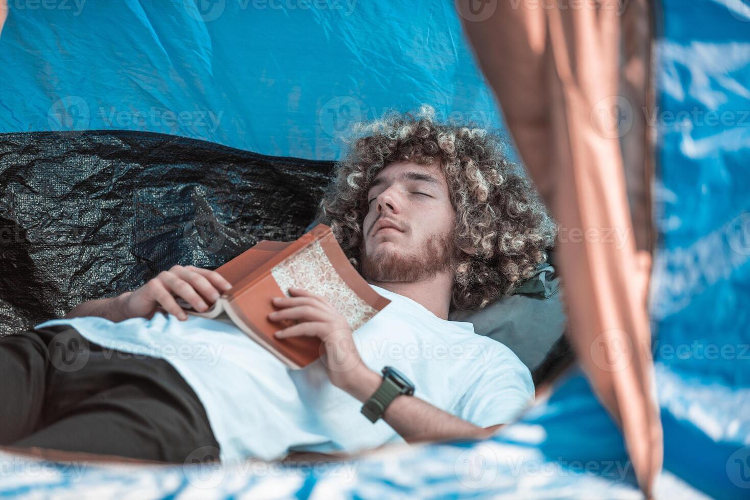 An afro teenager relaxes in a mountaineering tent while reading a book photo
