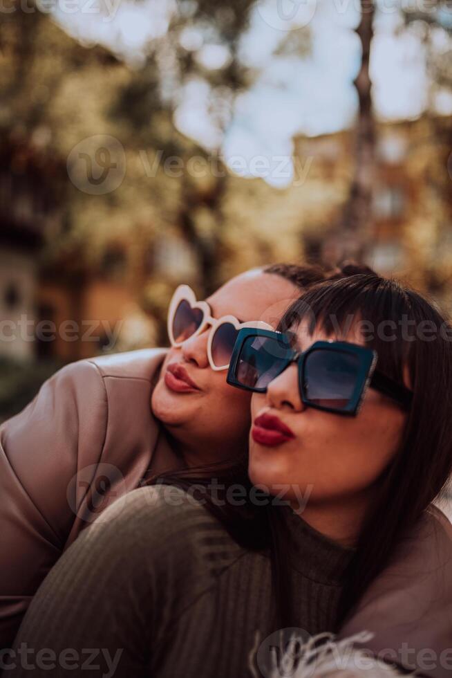 Two young women embrace each other emotionally outside on a sunny day while wearing sunglasses photo