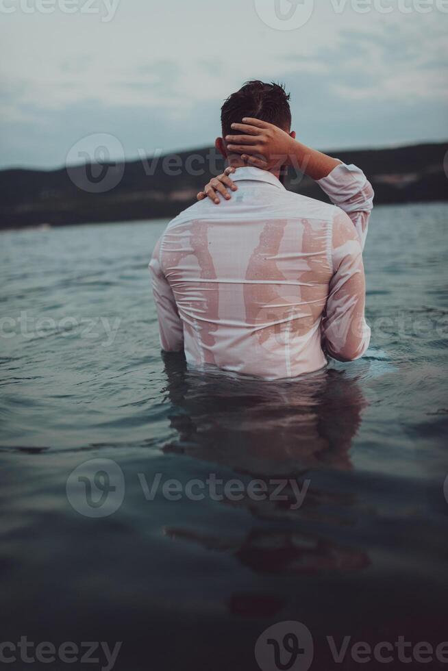 A symbolic and emotionally connected couple tenderly embraces against the backdrop of a serene sea, bathed in the warm hues of a breathtaking sunset photo