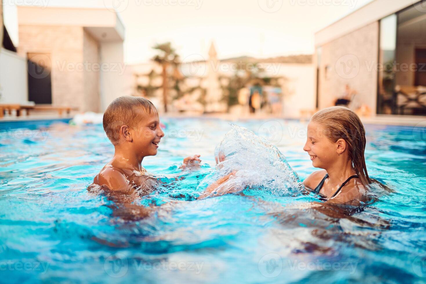 In a sunlit modern villa, a young brother and sister joyfully splash and play in the pool, basking in the warmth of a perfect summer day photo