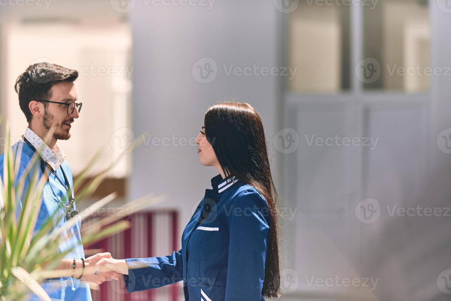 A doctor and a nurse share a friendly handshake in the hallway of a large, modern hospital, symbolizing collaboration, trust, and dedication in healthcare photo