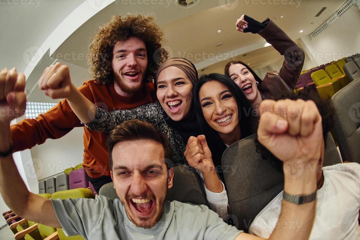 A diverse group of young people exuberantly celebrates and cheers while watching a soccer match, radiating excitement, unity, and sportsmanship photo