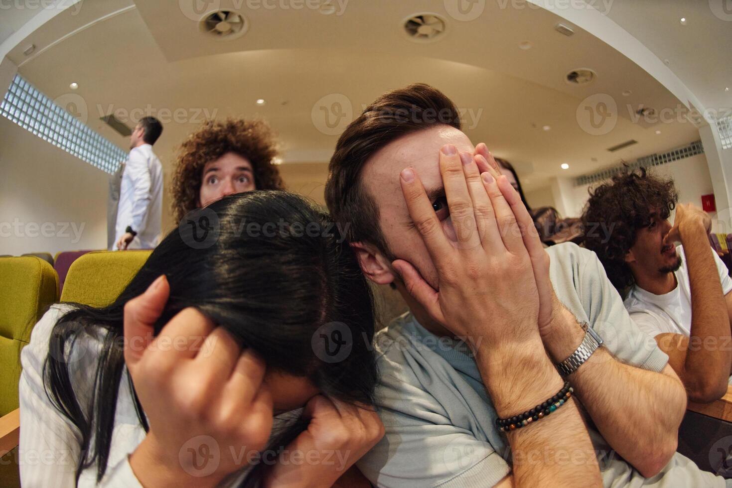 A diverse group of young people watches a thrilling movie in a cinema, their fearful expressions adding to the collective excitement and suspense of the horror film photo