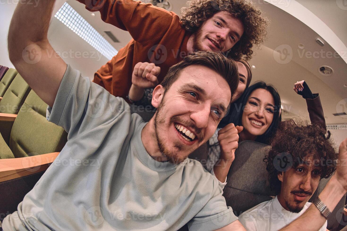 A diverse group of young people exuberantly celebrates and cheers while watching a soccer match, radiating excitement, unity, and sportsmanship photo