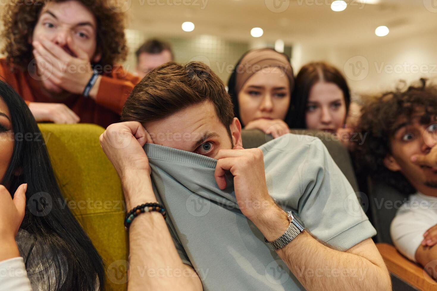 A diverse group of young people watches a thrilling movie in a cinema, their fearful expressions adding to the collective excitement and suspense of the horror film photo
