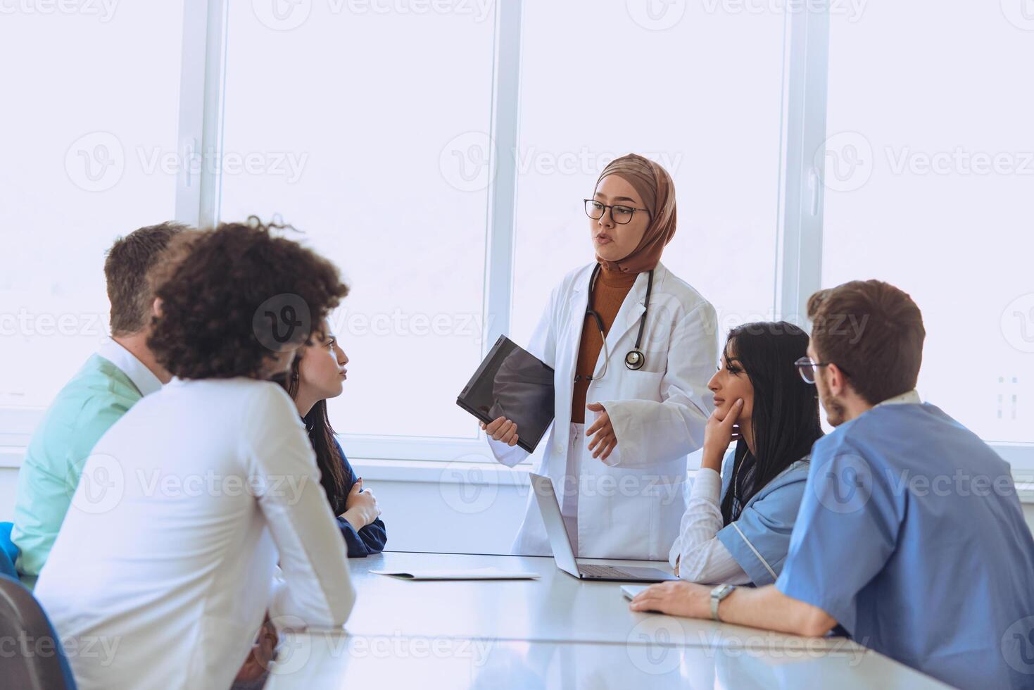 A successful doctor in a hijab confidently presents her work plan to colleagues in a hospital, while using a smart tablet to enhance patient care and communication in the healthcare facility photo